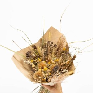 Bouquet de fleurs séchées dans les tons jaune marron tenu par une main