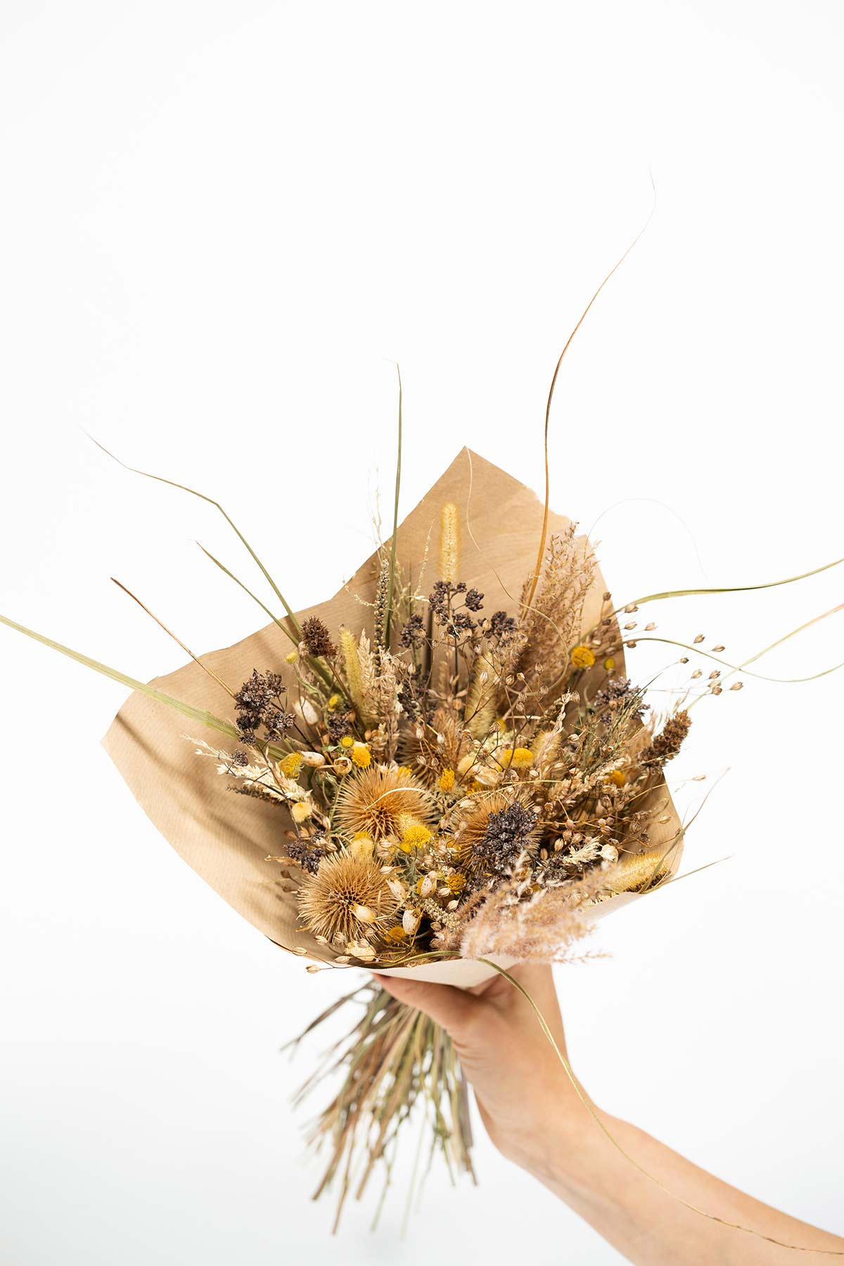 Bouquet de fleurs séchées dans les tons jaune marron tenu par une main
