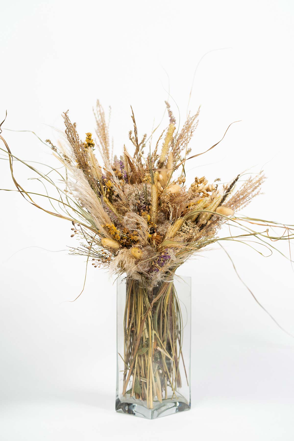 Gros bouquet de fleurs sauvages séchées dans un vase rectangulaire en verre transparent