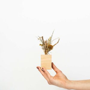Petit socle en bois type soliflore contenant un mini bouquet de fleurs séchées et tenu par une main