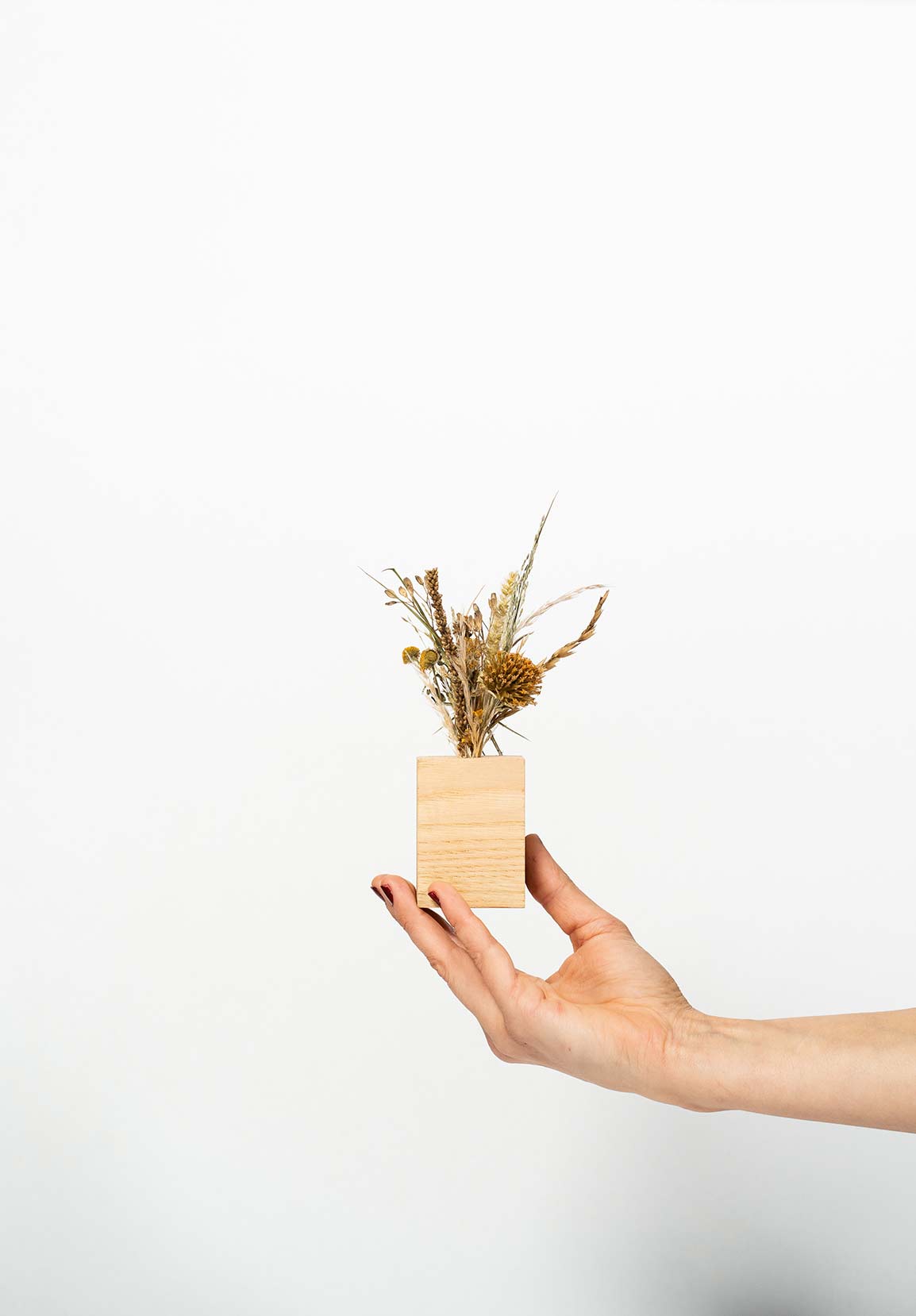Petit socle en bois type soliflore contenant un mini bouquet de fleurs séchées et tenu par une main