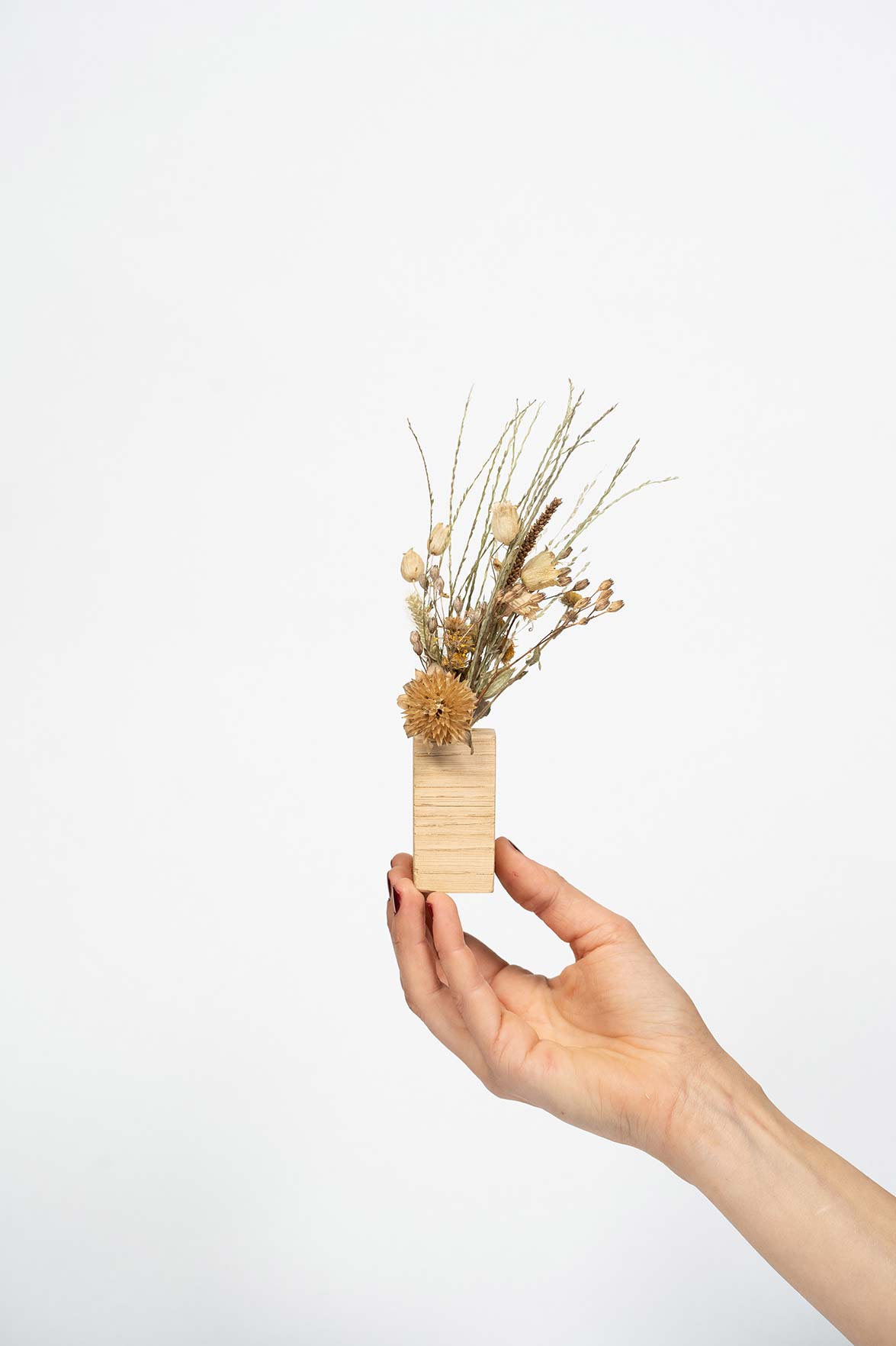 Petit socle en bois type soliflore contenant des fleurs séchées et tenu par une main
