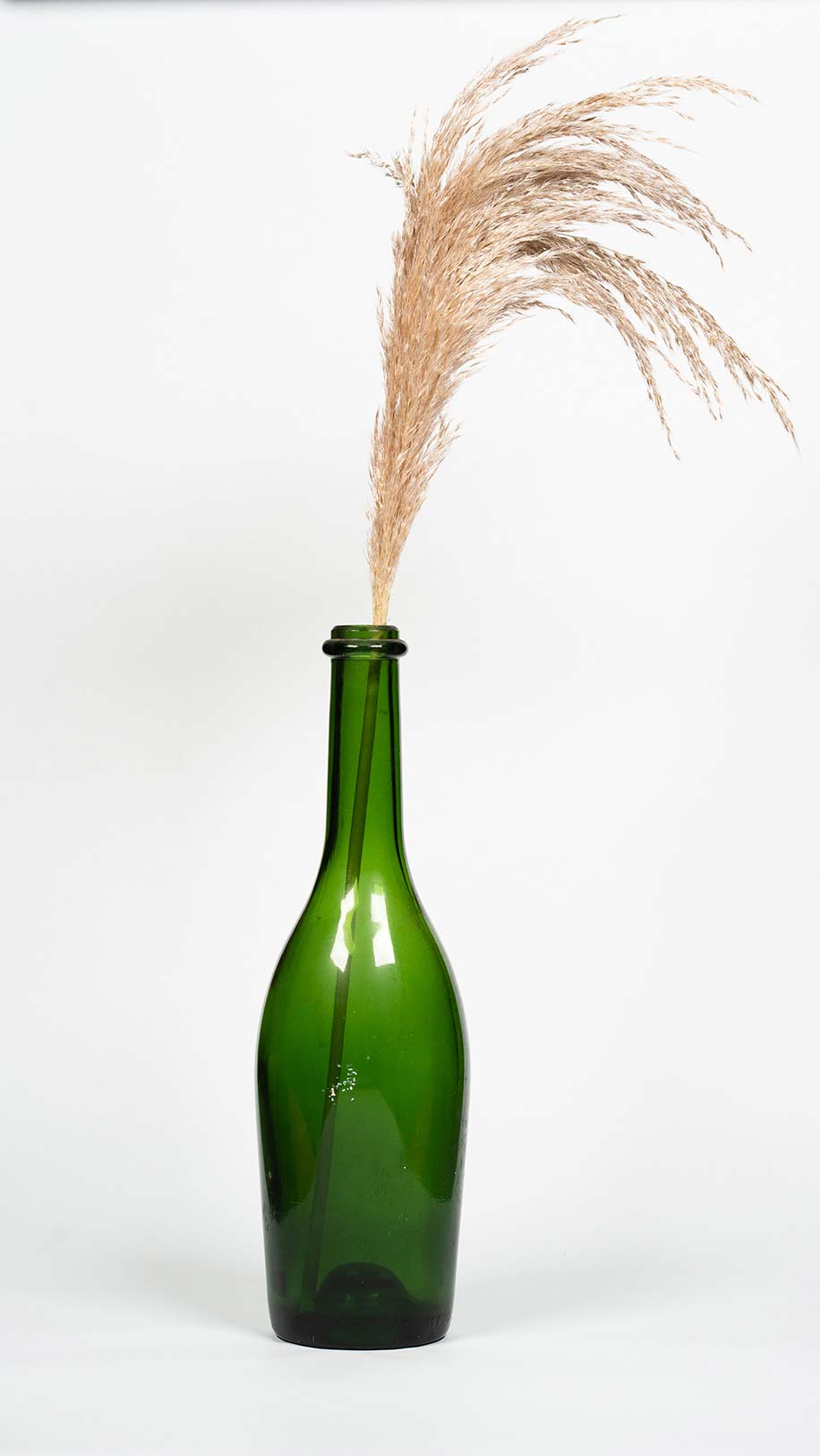Vase en verre type gross bouteille verte contenant des fleurs séchées type pampas