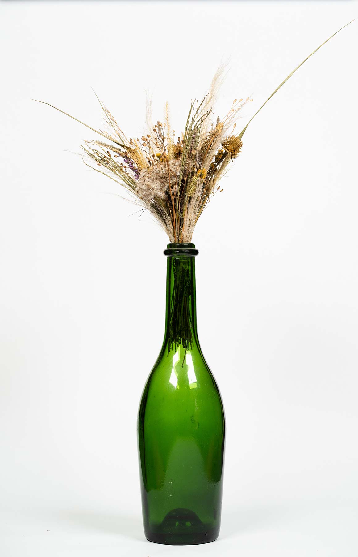 Vase en verre type gross bouteille verte contenant un bouquet de fleurs séchées