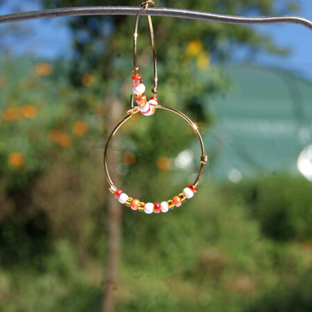 Paire de boucles d'oreilles de type créole ornées de perles de rocaille en verre orange jaune blanc rouge sur fond blanc