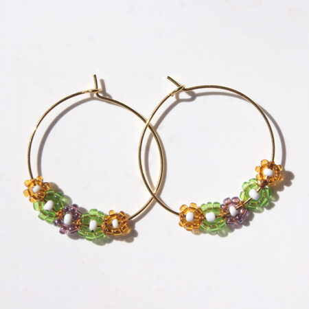 Paire de boucles d'oreilles de type créole ornées de fleurs en perles vert jaune et violet sur fond blanc