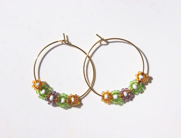 Paire de boucles d'oreilles de type créole ornées de fleurs en perles vert jaune et violet sur fond blanc